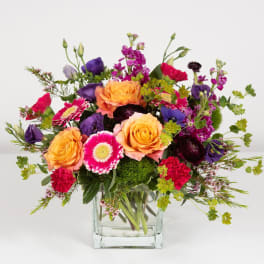 Mixed bouquet of orange, pink, and purple flowers in a clear glass vase