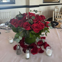 Red rose centerpiece in a glass vase with scattered petals