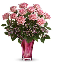 Pink roses arranged in a tall glass vase with small purple filler flowers