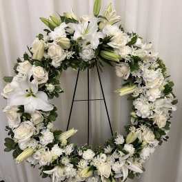 White floral wreath on a black stand with roses and lilies
