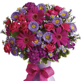 Pink roses and purple daisies in a lavender vase with a ribbon