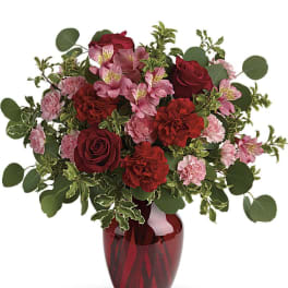 Red roses and pink flowers arranged in a red glass vase