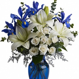 White lilies, blue irises, and white roses in a blue glass vase