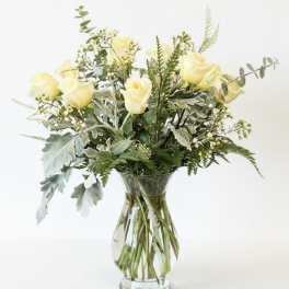 Yellow roses arranged in a clear glass vase with mixed greenery