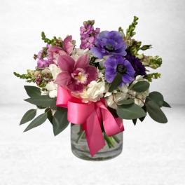 Pink and purple flowers arranged in a glass vase with a bright pink ribbon