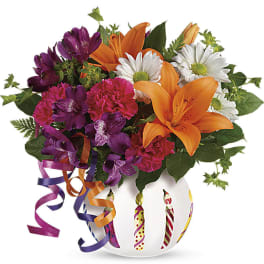 Colorful bouquet of orange lilies, purple alstroemeria, pink carnations, and white daisies in a round candle-print vase