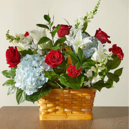 Basket arrangement of red roses, white lilies, and blue hydrangeas