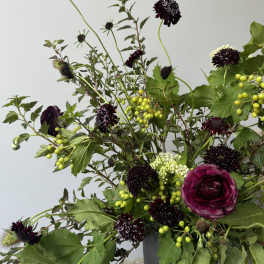 Dark purple flowers and green berries in a gray vase