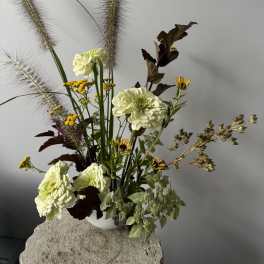Tall floral arrangement with pale green blooms and feathery grasses in a white vase