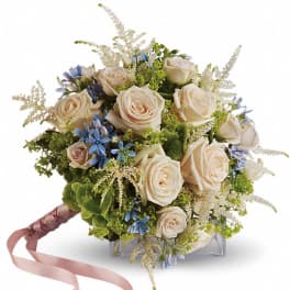 Cream roses and blue flowers in a hand-tied bouquet with a pink ribbon