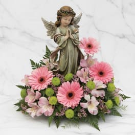 Pink gerbera daisies and lilies arranged around an angel figurine