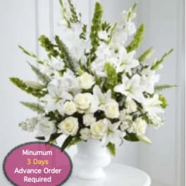 White floral arrangement in a white pedestal vase with tall green accents