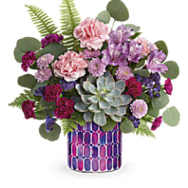 Mixed pink and purple flowers in a patterned vase with a succulent centerpiece
