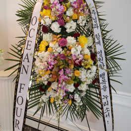 Tall standing floral wreath with white ribbons and mixed blooms