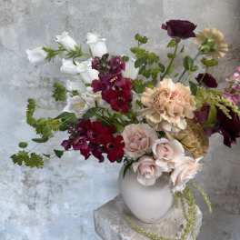 Mixed bouquet of roses, carnations, and white bell-shaped flowers in a white vase