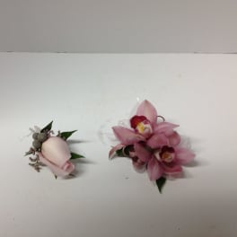 Two small pink floral corsages on a white surface