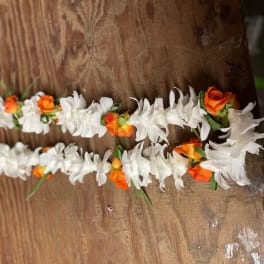 Two white and orange flower garlands laid on a wooden surface