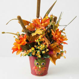 Autumn floral arrangement in a red owl pot with orange flowers and cattails
