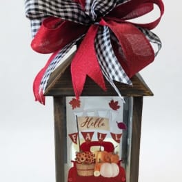 Wooden lantern with a large red and black plaid bow and fall-themed insert