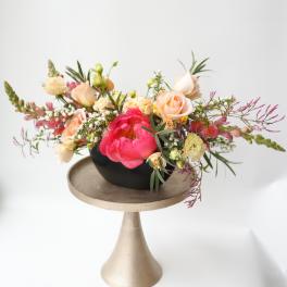 Mixed bouquet of peach and pink flowers in a black bowl on a pedestal stand
