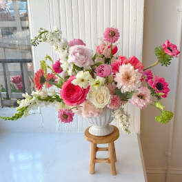 Mixed pink and white flower arrangement in a white vase on a wooden stool