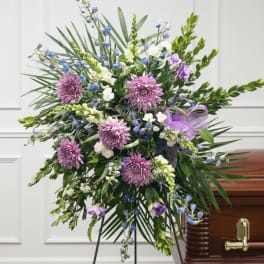 Large funeral spray with purple and blue flowers on a stand beside a casket