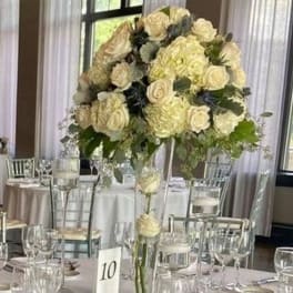 Tall cream rose centerpiece in a clear glass vase on a banquet table