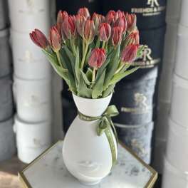 Red tulips arranged in a white face-shaped vase with a green ribbon