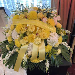 Yellow and white funeral spray with ribbon on a casket