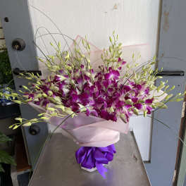 Bouquet of purple and white orchids wrapped in pink paper with a purple ribbon