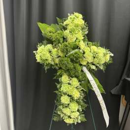 Green floral standing cross with a white ribbon on an easel