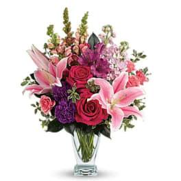 Pink lilies, roses, and purple flowers in a clear glass vase