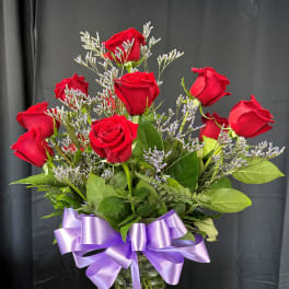 Red roses in a glass vase with a purple ribbon
