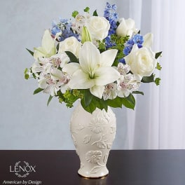 White lilies and roses arranged in a decorative vase with blue accents