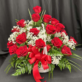 Red roses arranged in a white basket with baby's breath and a red ribbon