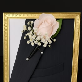 Boutonniere with a pale pink rose and white baby's breath in a gold frame