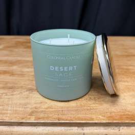A sage green candle in a metal tin with its lid beside it
