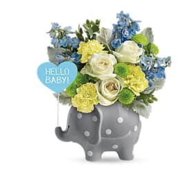 Bouquet of blue, white, and yellow flowers in a gray elephant planter with a baby sign
