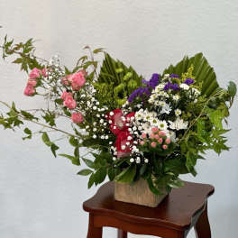 Mixed bouquet of pink and red roses with white and purple filler flowers in a wooden container