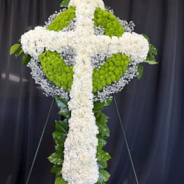 White and green floral cross on a stand against a dark backdrop