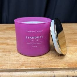 Pink candle in a glass jar with a metal lid on a wooden surface.