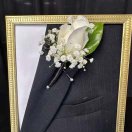 White boutonniere pinned to a black suit in a gold frame