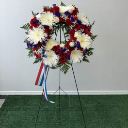 Circular red, white, and blue floral wreath on a stand