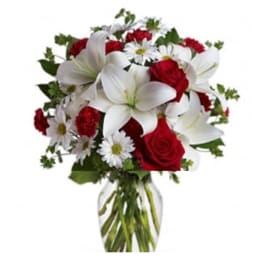 Bouquet of red roses, white lilies, and white daisies in a clear vase