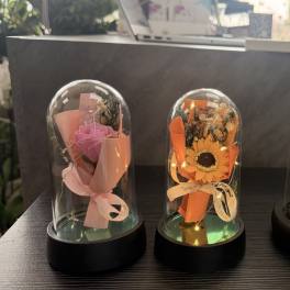 Three small flower gifts displayed under clear domes on a table