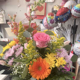 Mixed bouquet in a clear glass vase with pink, orange, yellow, and lavender flowers