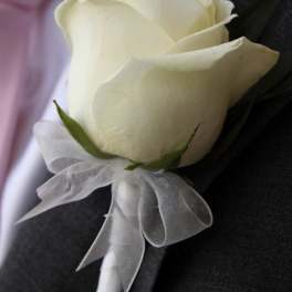 White rose boutonniere with a sheer ribbon on a dark suit lapel