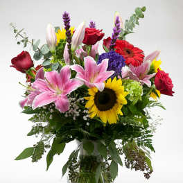 Mixed bouquet of lilies, roses, and sunflowers in a glass vase