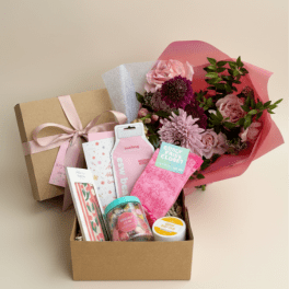 Pink flower bouquet beside a gift box filled with small packaged items