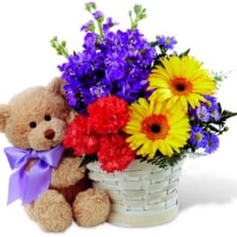 Teddy bear beside a basket of colorful flowers